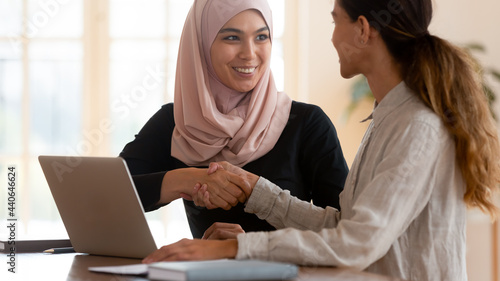 Smiling Asian muslim businesswoman wearing hijab shaking client hand after successful deal close up, congratulating, satisfied hr manager hiring new employee, business partners handshaking at meeting