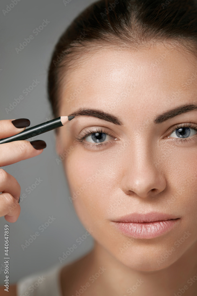 Eyebrow makeup. Beautiful model shaping brows with brow pencil closeup. Beauty woman with professional makeup contouring eyebrows