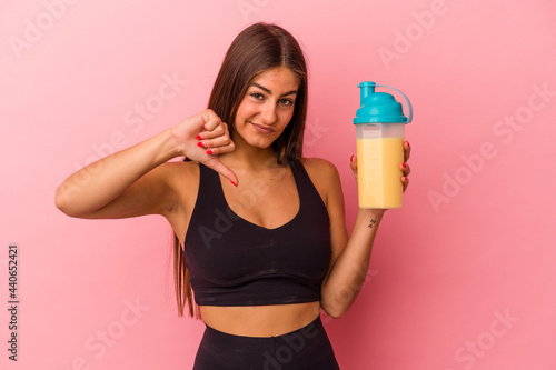 Young caucasian woman holding a protein shake isolated on yellow background showing a dislike gesture, thumbs down. Disagreement concept.