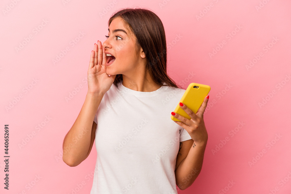 Young caucasian woman holding a mobile phone isolated on pink background shouting and holding palm near opened mouth. Young caucasian woman holding a mobile phone isolated on pink background shouting and holding palm near opened mouth.