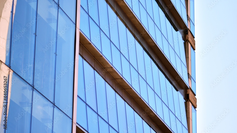 Abstract closeup of the glass-clad facade of a modern building covered in reflective plate glass. Architecture abstract background. Glass wall and facade detail. Abstract closeup of the glass-clad facade of a modern building covered in reflective plate glass. Architecture abstract background. Glass wall and facade detail.