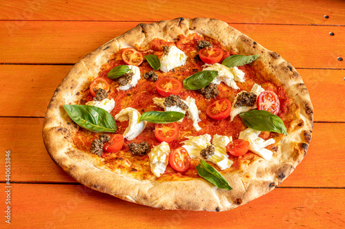 Italian sponge crust pizza with pieces of bufala cheese, cherry tomatoes, trozos de carne and lots of basil leaves