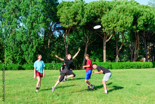 Group of mixed young teenagers people in casual wear playing with plastic flying disc game in a park oudoors. jumping woman catch a disk to a teammate in a match. milennial friends outside in a garden