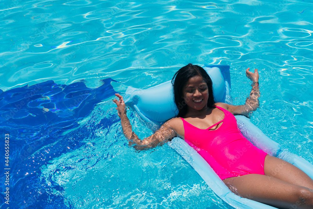 Smiling young girl in bikini having fun on inflatable in swimming pool. Woman sunbathing at a tropical vacation party. Cute black woman under the sun.