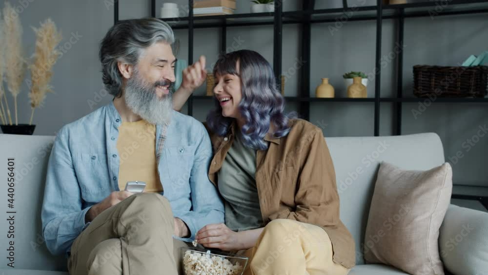 Happy couple watching TV talking and laughing eating popcorn sitting on couch in living room. Modern technology and family lifestyle concept. Happy couple watching TV talking and laughing eating popcorn sitting on couch in living room. Modern technology and family lifestyle concept.