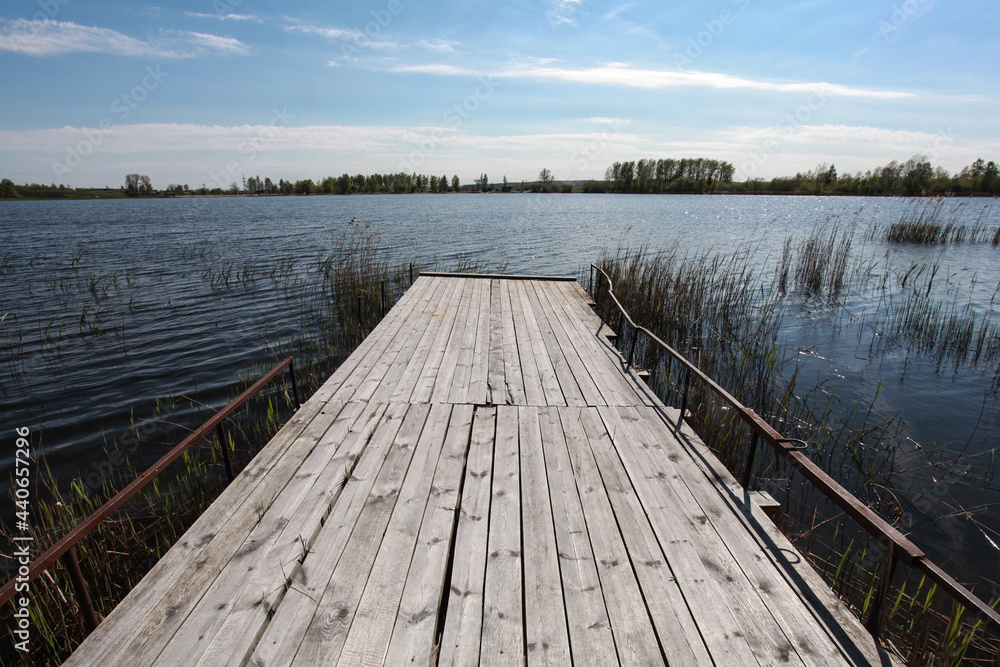 Wooden pier and grass on lake shore on sunny summer day