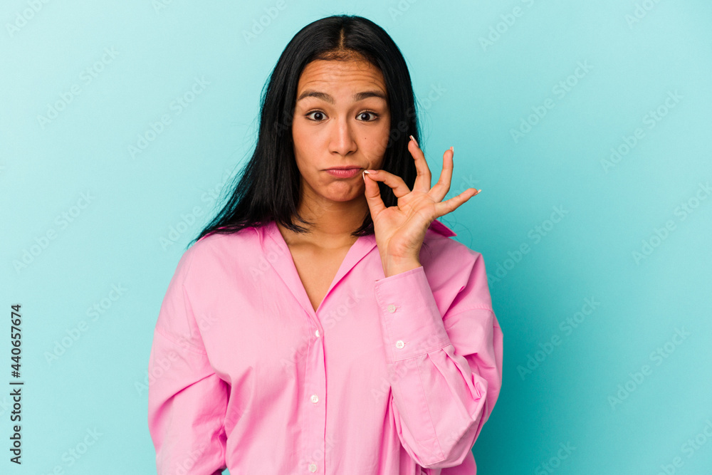 Young Venezuelan woman isolated on blue background with fingers on lips keeping a secret. Young Venezuelan woman isolated on blue background with fingers on lips keeping a secret.