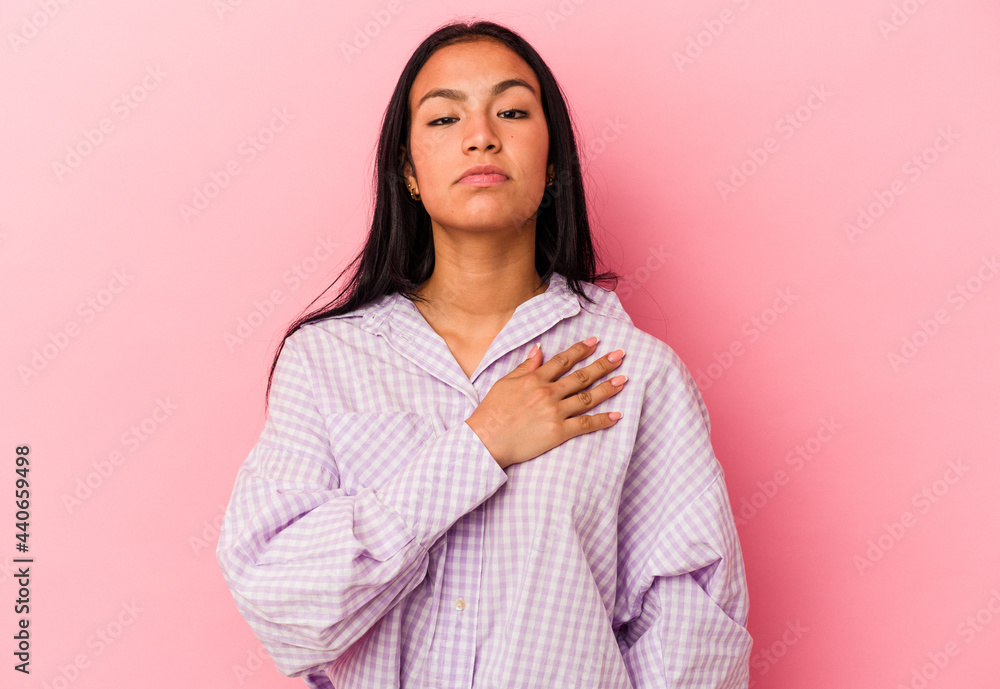 Fototapeta premium Young Venezuelan woman isolated on pink background taking an oath, putting hand on chest.