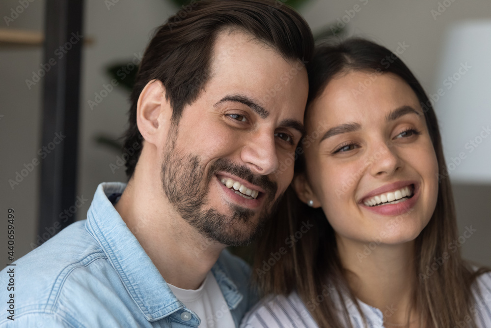 Close up head shot beautiful young happy family couple looking in distance, dreaming of new beginning or planning future. Affectionate loving man and woman enjoying peaceful tranquil moment at home. Close up head shot beautiful young happy family couple looking in distance, dreaming of new beginning or planning future. Affectionate loving man and woman enjoying peaceful tranquil moment at home.