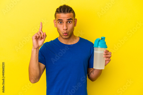 Young venezuelan man drinking a protein shake isolated on yellow background having some great idea, concept of creativity.