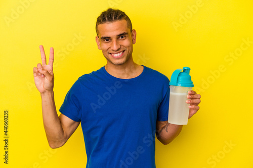 Young venezuelan man drinking a protein shake isolated on yellow background joyful and carefree showing a peace symbol with fingers.