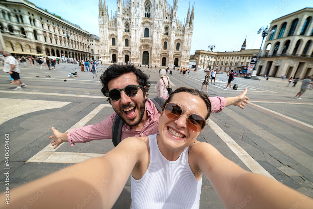 friends couple taking a selfie in front of a famous landmark - Tourists photographing the Duomo cathedral in Milan - happy tourist people on vacation sightseeing the city Milano