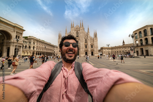 handsome man taking a selfie in front of a famous landmark - Tourists photographing the Duomo cathedral in Milan - happy tourist people on vacation sightseeing the city Milano