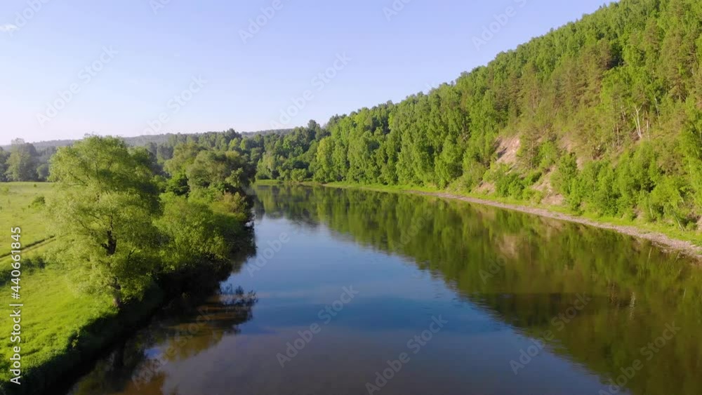 Aerial view of the river, South Ural, Russia. A stormy wide river of dark color flows between a high hill with dense lush green trees and a low meadow. Small gray clouds move in the blue sky. Summer Aerial view of the river, South Ural, Russia. A stormy wide river of dark color flows between a high hill with dense lush green trees and a low meadow. Small gray clouds move in the blue sky. Summer
