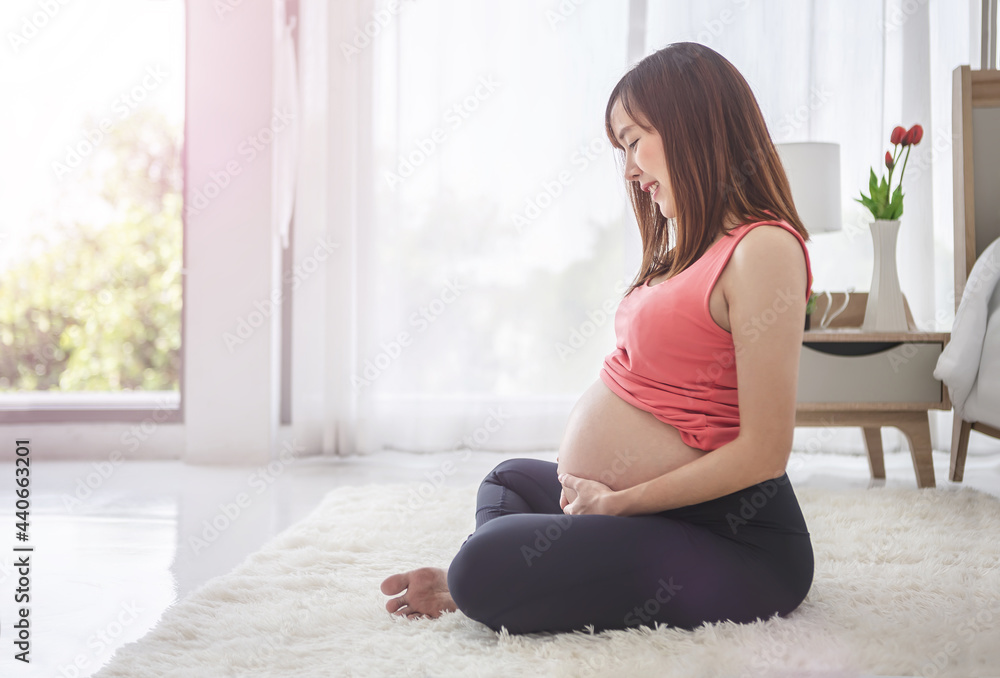 Pregnant woman sitting on the floor taking care of her child by holding baby in her pregnant belly in the bedroom