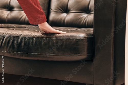 Caucasian woman in the store chooses to buy an expensive sofa made of brown leather. The concept of buying new home furniture, interior design and decor. Hands close up shot