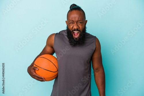 African american man playing basketball isolated on blue background screaming very angry and aggressive. © Asier