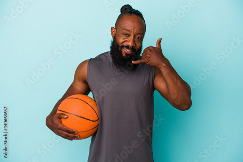 African american man playing basketball isolated on blue background showing a mobile phone call gesture with fingers. © Asier