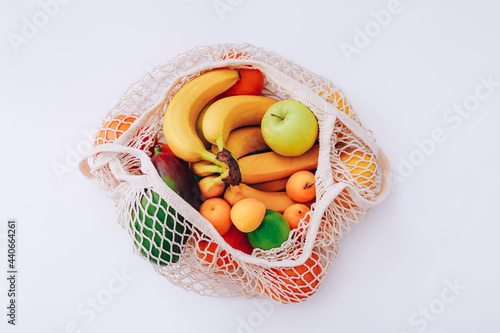 Cotton mesh bag with fresh colorful fruits on light background, top view. Zero waste concept