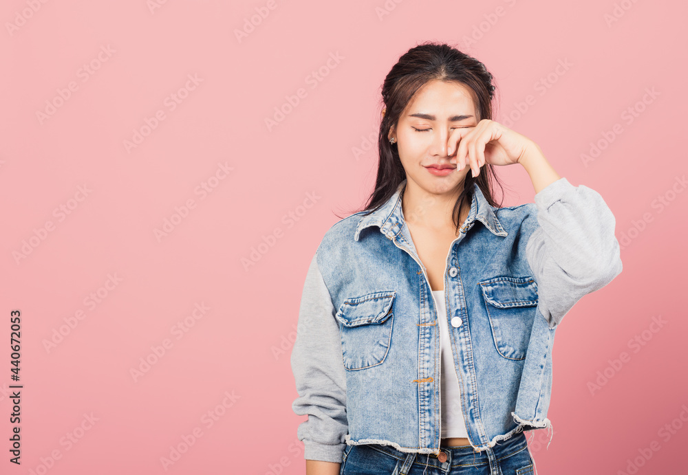 Asian portrait beautiful cute young woman wear denim bad mood her cry wipe tears with fingers, studio shot isolated on pink background, Thai female feeling sad unhappy crying with copy space Asian portrait beautiful cute young woman wear denim bad mood her cry wipe tears with fingers, studio shot isolated on pink background, Thai female feeling sad unhappy crying with copy space