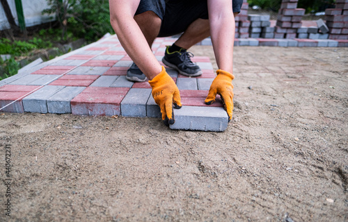 mason makes a pedestrian path. A worker is laying paving stones. The hands of a worker lay stones on the sand.