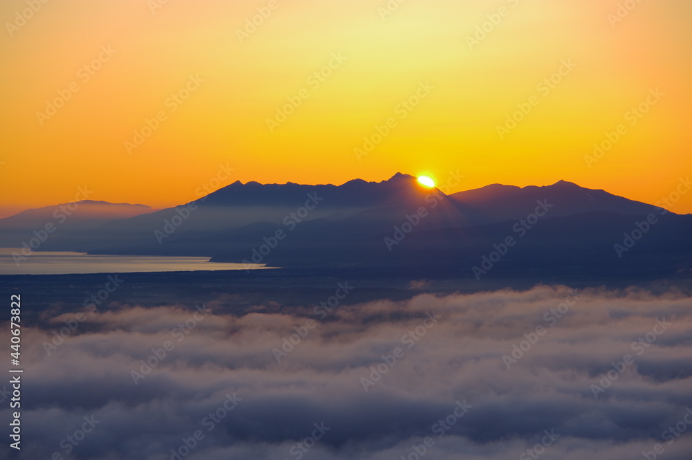 快晴の空に眩しく輝く朝陽に照らされた雲海とシルエットの際立つ遠くの山。