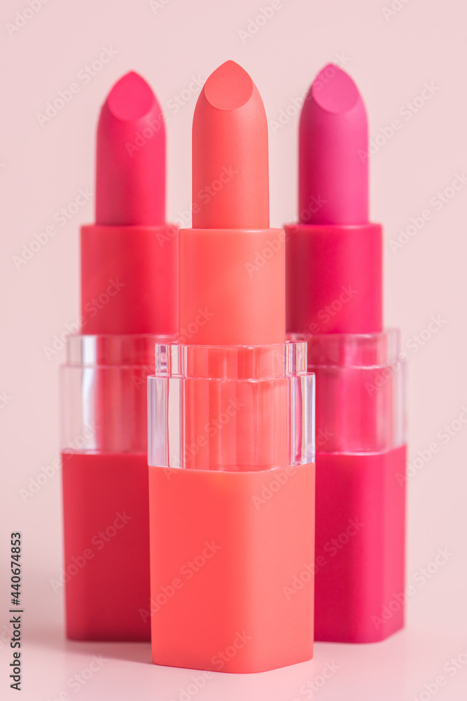 Set of three color lipsticks. Wine lipstick, pink lipstick and orange lipstick in colourful lid on a pink background background. Photo of Vivid decorative cosmetics for lips. Set of three color lipsticks. Wine lipstick, pink lipstick and orange lipstick in colourful lid on a pink background background. Photo of Vivid decorative cosmetics for lips.