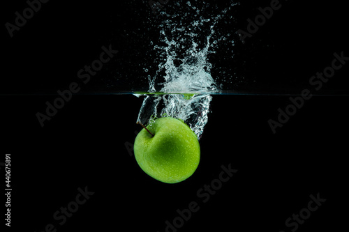 Green apple falling in water with splash on black background.