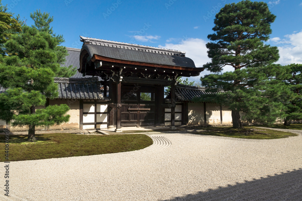 Sunlit stone zen garden with raked gravel an gate at Sogenchi garden at Tenryu-ji temple in Kyoto, Japan
