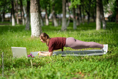 Young girl having online workout outdoors using laptop. Pilates or yoga video lesson on internet. Happy smiling girl practicing pilates lesson online in garden outdoors during quarantine