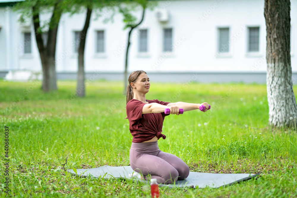 beautiful, smiling blonde girl holding dumbbells in her hands, doing sports in the fresh air beautiful, smiling blonde girl holding dumbbells in her hands, doing sports in the fresh air