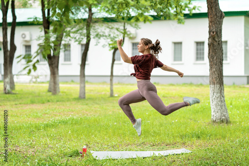 beautiful girl athlete in sportswear jumps high in the park or in the yard of her house