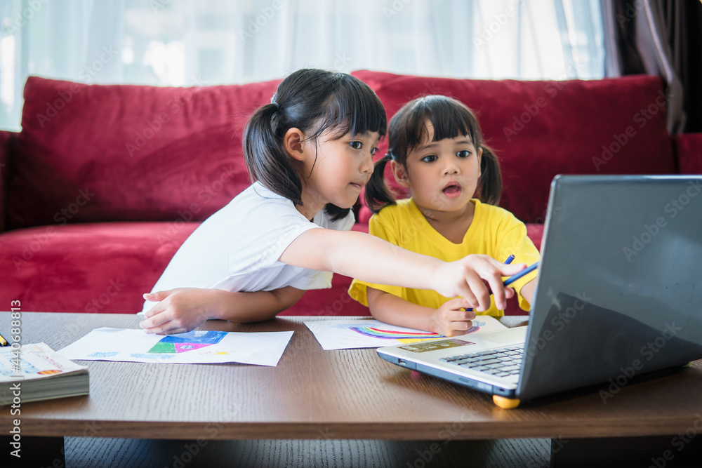 Two asian child girl students study online with teacher by video call together. Siblings are homeschooling with computer laptop during quarantine due to Covid 19 pandemic. Two asian child girl students study online with teacher by video call together. Siblings are homeschooling with computer laptop during quarantine due to Covid 19 pandemic.