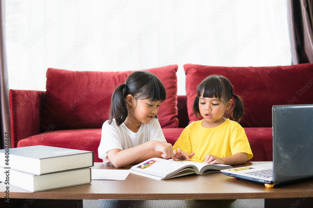 Two asian child girl students study online with teacher by video call together. Siblings are homeschooling with computer laptop during quarantine due to Covid 19 pandemic.