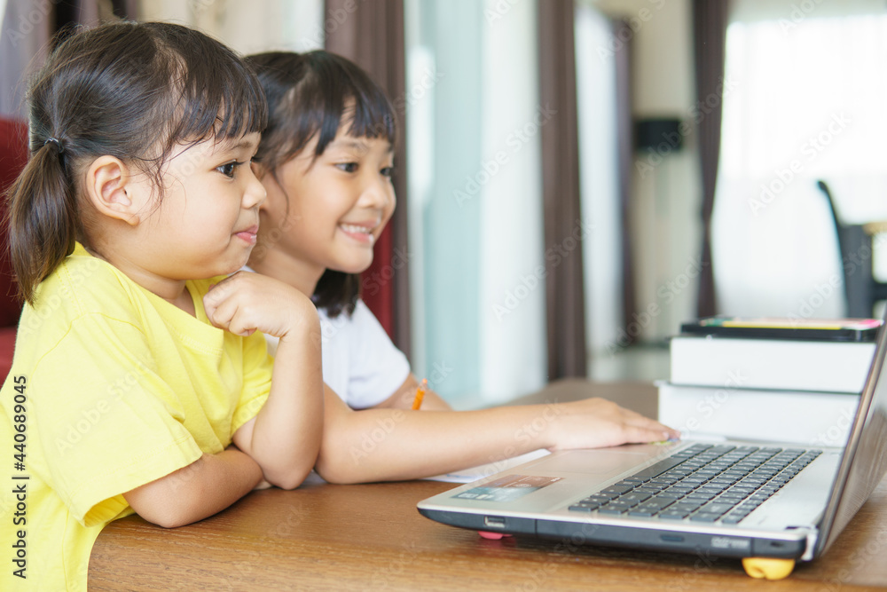 Two asian child girl students study online with teacher by video call together. Siblings are homeschooling with computer laptop during quarantine due to Covid 19 pandemic.