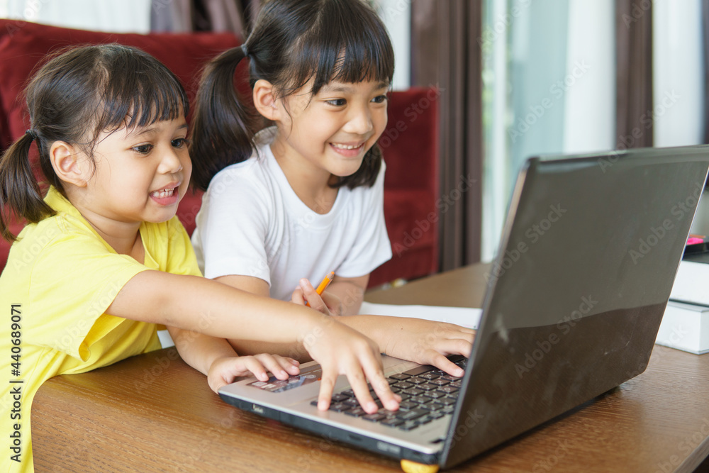 Two asian child girl students study online with teacher by video call together. Siblings are homeschooling with computer laptop during quarantine due to Covid 19 pandemic. Two asian child girl students study online with teacher by video call together. Siblings are homeschooling with computer laptop during quarantine due to Covid 19 pandemic.