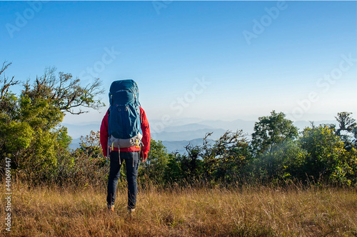 Young traveler wearing red sweater and green backpack standing and watched beautiful view on top of the mountain. He is happy to be with herself and stay with nature. © Tarokmew