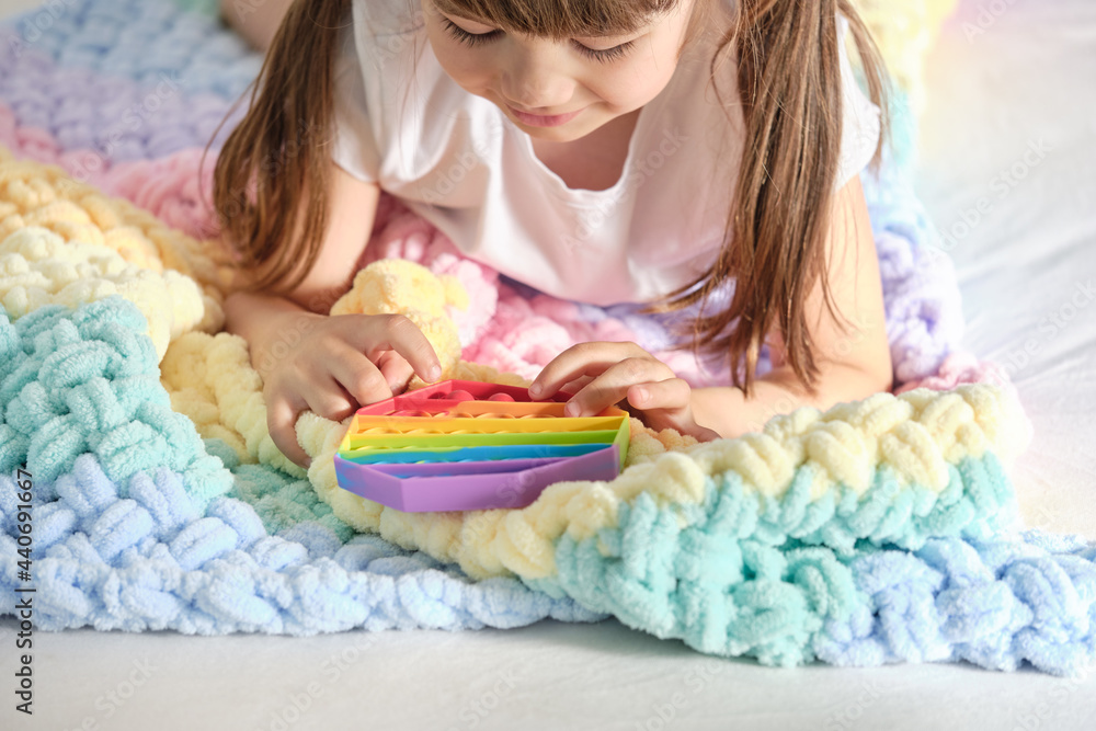 little cheerful girl plays in a multi-colored plastic toy pop it while lying on the bed. playing at home during summer holidays little cheerful girl plays in a multi-colored plastic toy pop it while lying on the bed. playing at home during summer holidays