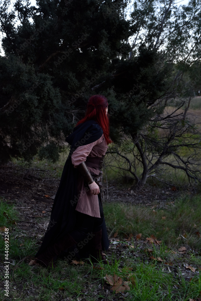 portrait of red haired girl wearing fantasy medieval clothes of a wandering adventurer. natural light in a woodland forest setting. portrait of red haired girl wearing fantasy medieval clothes of a wandering adventurer. natural light in a woodland forest setting.