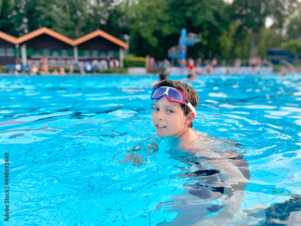 School kid boy splashing in an outdoor swimming pool on warm summer day. Happy healthy preteen child enjoying sunny weather in city public pool. Kids activity outdoors with water.