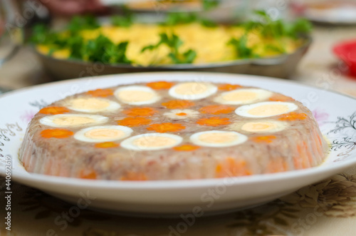 Aspic meat jelly on a white plate close-up, decorated with chicken eggs and carrots in the form of flowers