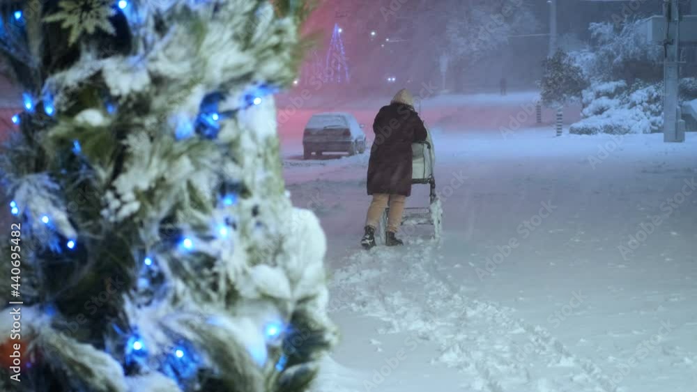 Hard storm in winter city. Woman with a stroller in heavy snow in the night city. Hard storm in winter city. Woman with a stroller in heavy snow in the night city.