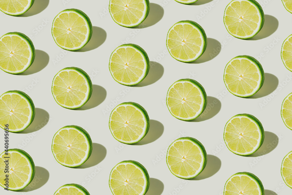Texture made with slices of lime isolated on a bright white background. A pattern of citrus fruit with summer shadows. Creative food concept. Flat lay, top view.