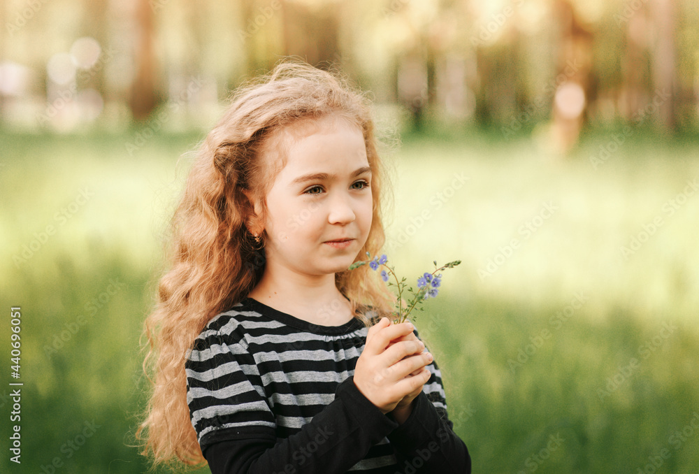 Little girl with curly hair in the park with a bouquet of wildflowers Little girl with curly hair in the park with a bouquet of wildflowers