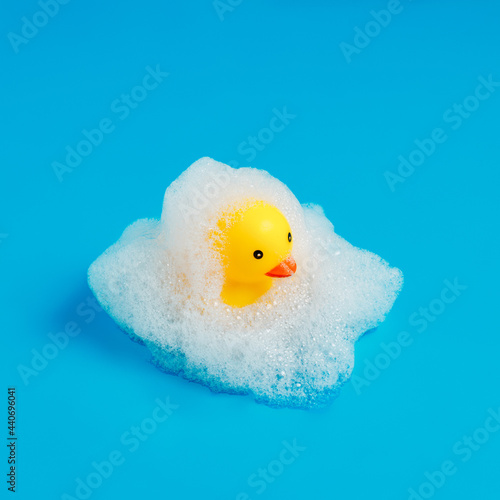 Fotografie Yellow duck rubber toy with foamy bubbles isolated on a bright blue background