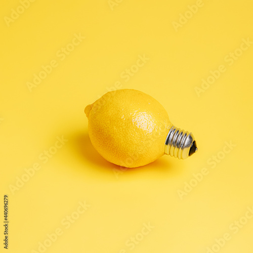 A single fresh lemon as a light bulb isolated on a bright yellow background. Trendy fruit idea. Abstract and surreal healthy diet. Creative food concept.