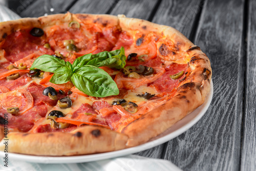 Fresh italian pizza with salami and black olives served over rustic wooden background. Traditional Italian pizza recipe