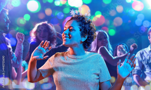 celebration and nightlife concept - happy smiling young african american woman dancing at christmas or new year party in ultraviolet neon lights over nightclub background