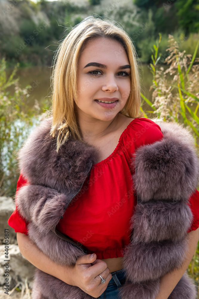 beautiful girl in a fur coat and a light red T-shirt and shorts posing by the lake beautiful girl in a fur coat and a light red T-shirt and shorts posing by the lake