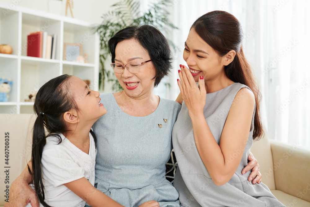 Mother and grandmother laughing at funny joke of preteen little girl, the are hugging and sitting on couch at home Mother and grandmother laughing at funny joke of preteen little girl, the are hugging and sitting on couch at home